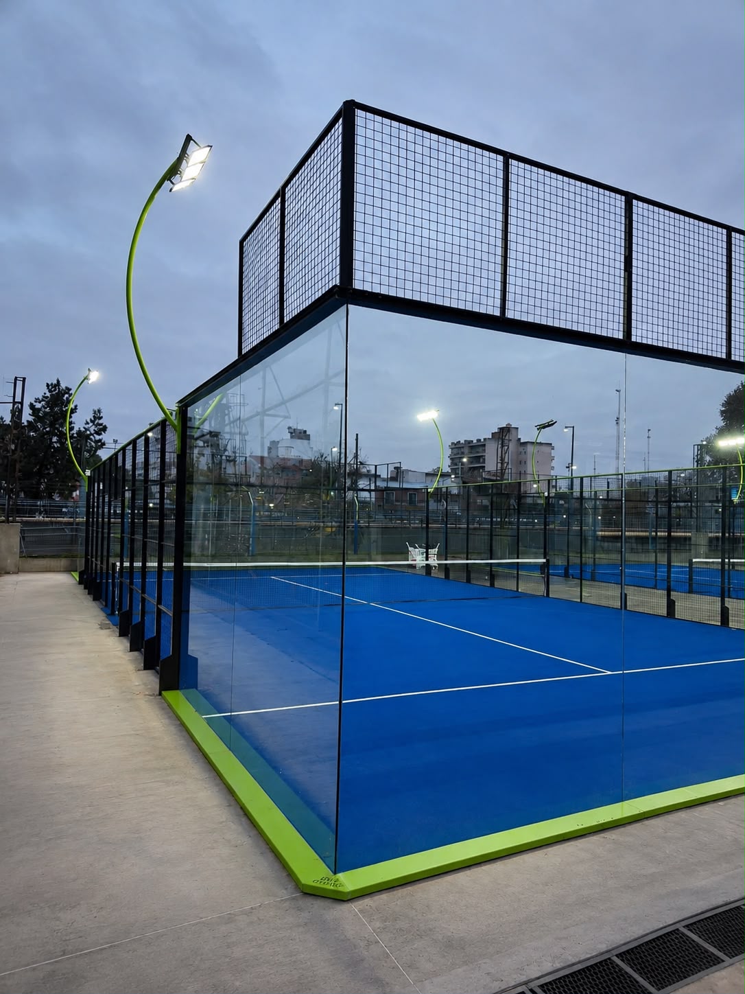 Cancha de pádel Blue Court al atardecer con superficie azul, paredes de vidrio y luces encendidas